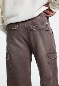 Stofbruine cargobroek met zijzakken, rafelige zakranden en een lichte glans. Gemaakt van denim met een zachte textuur.