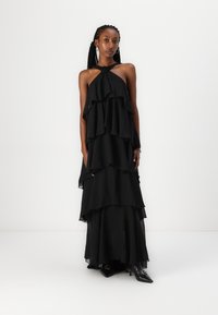 Rochie maxi neagră, cu guler halter, confecționată dintr-un material ușor, având straturi volănuțe și o siluetă fluidă.