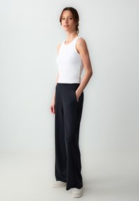 Witte tanktop gecombineerd met hoge zwarte wijde broek met zijzakken, van soepel materiaal, en lage witte sneakers.