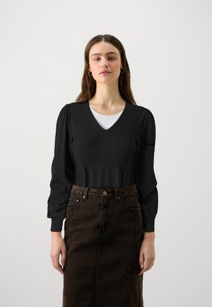 Schwarzer Strickpullover mit V-Ausschnitt und gerippter Textur, kombiniert mit einem hoch taillierten, dunkelbraunen Jeansrock. Einfaches, figurbetontes Design.