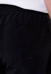 Pantalons noirs à taille élastique avec une texture lisse, dotés d'une poche visible et de détails en rivet. Présentés de dos, mettant en valeur les éléments de design.