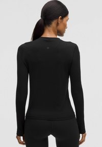 Črn dolgesleevni top s prilegajočim krojem, izdelan iz gladkega materiala. Ima subtilen logotip zadaj in okrogel izrez.