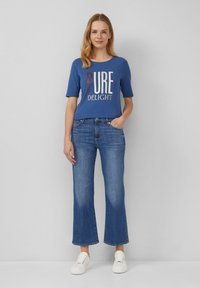 T-shirt bleu avec le graphique "PURE DELIGHT", associé à un jean flare bleu clair et des baskets blanches. Tissu doux et coupe décontractée.
