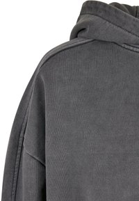 Sweat à capuche gris avec un tissu doux et texturé. Comprend une capuche avec cordon de serrage et une coupe décontractée. Coutures visibles le long des épaules et des côtés.