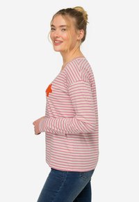 Camisa de manga larga a rayas rosa y blanca, con un aplique de estrella naranja en el pecho. La tela parece suave y tiene un corte holgado.