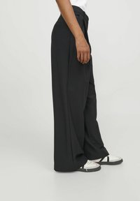 Zwarte wijde broek van gladde stof, met een hoge taille, zijzakken en gecombineerd met witte sneakers.