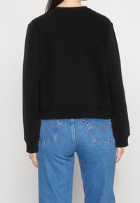 Sudadera negra con cuello redondo, puños y dobladillo acanalados, combinada con jeans de mezclilla azul claro de talle alto con bolsillos parche.