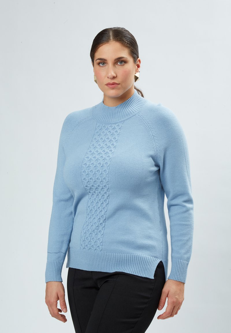 Lyseblå strikket sweater med ribbet høj Hals, tekstureret midterpanel og sidespalter, sammen med sorte bukser. Sømløse ærmer.