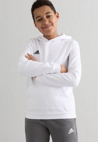 Hvid hættetrøje med sort Adidas-logo på brystet, kombineret med grå sweatpants med et lille hvidt logo. Glat stofstruktur.
