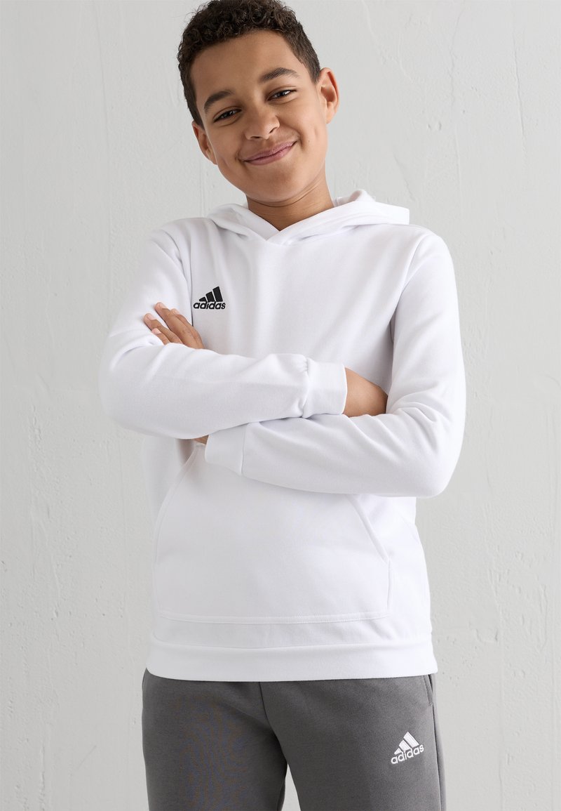 Hvid hættetrøje med sort Adidas-logo på brystet, kombineret med grå sweatpants med et lille hvidt logo. Glat stofstruktur.