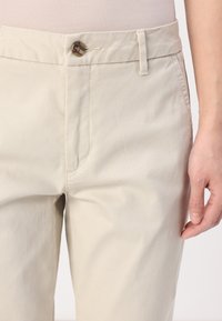 Beige puuvillahousut, joissa on sileä pinta, etupainike suljenta, sivutaskut ja kapea malli.