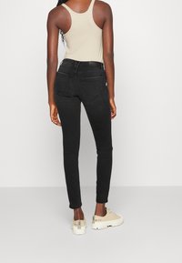 Jeans skinnies negros de cintura alta, con costuras detalladas y dos bolsillos traseros. Combinados con zapatillas beige y una camiseta sin mangas ligera.