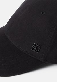 Cappello nero realizzato in tessuto testurizzato, con visiera curvata e una piccola etichetta con logo nera sul lato. Design semplice ed elegante.