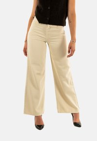 Pantalones de pierna ancha color crema en un tejido texturizado, con una cintura alta y costuras laterales. Combinados con tacones altos negros.