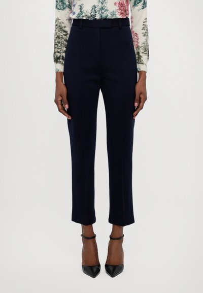 Pantalons navy ajustés avec une texture lisse, coupe slim et longueur chevilles. Stylés avec des escarpins noirs et un haut à motifs.