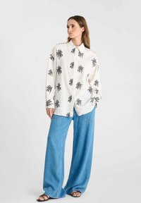 White button-up shirt with black palm tree pattern, paired with wide-leg blue denim pants. The fabric appears lightweight and casual.
