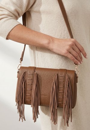 Bruine leren schoudertas met lange franjes, vastgehouden door een persoon die een beige top met lange mouwen en een jurk draagt.