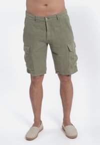 Pantaloni cargo in lino verde con chiusura a bottone, dotati di due tasche laterali e una vestibilità comoda, mostrati con scarpe espadrillas a righe.