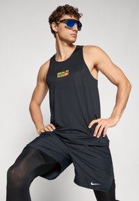 Schwarzes ärmelloses Sporttanktop mit "BERLIN RUN"-Logo in Gelb und Rot, kombiniert mit schwarzen Shorts und schwarzen Leggings, die das Nike-Logo tragen.