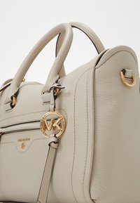 Jasnobeżowa, teksturowana skórzana torebka z dwoma uchwytami, przednią kieszenią na zamek błyskawiczny oraz złotym logo Michael Kors i akcentami.