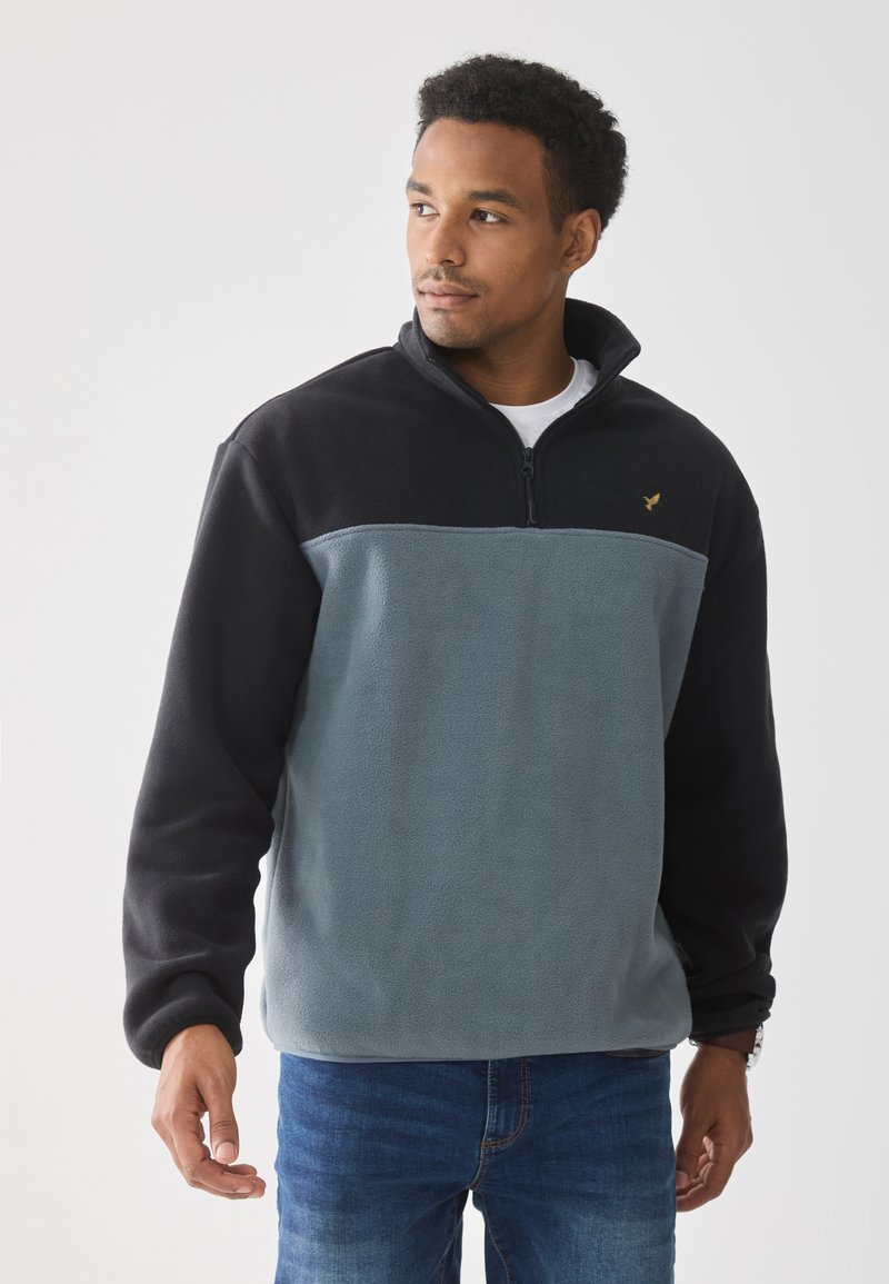 Sudadera de forro polar en azul claro y negro. Cuello con cremallera, mangas largas, tejido texturizado, con un pequeño logo dorado en el pecho. Ajuste casual.