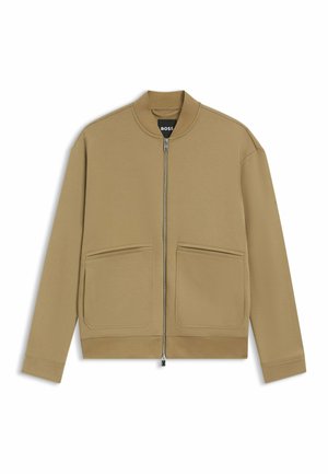 Giacca bomber color cammello con zip frontale, collo tondo, due tasche frontali e polsini a costine. Realizzata in tessuto morbido e liscio.
