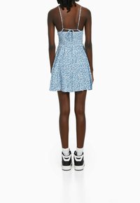 Modrá květinová šaty s přiléhavým trupem a rozšířenou suknią; obsahuje nastavitelné ramínka a nařasený zadní díl. Nosené s vysokými teniskami.