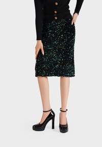 Maglione nero a coste con dettagli di bottoni, abbinato a una gonna lunga fino al ginocchio in paillettes nera e verde e tacchi a piattaforma neri lucidi con cinturini alla caviglia.