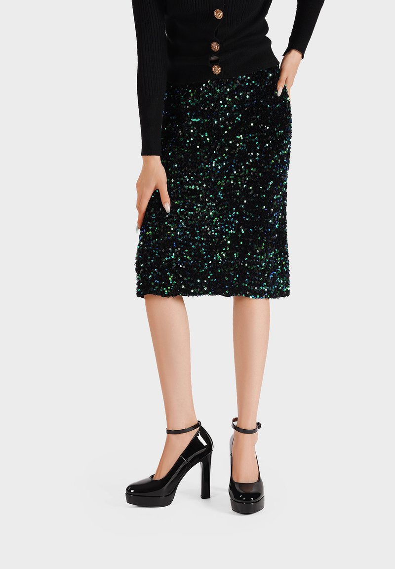 Maglione nero a coste con dettagli di bottoni, abbinato a una gonna lunga fino al ginocchio in paillettes nera e verde e tacchi a piattaforma neri lucidi con cinturini alla caviglia.