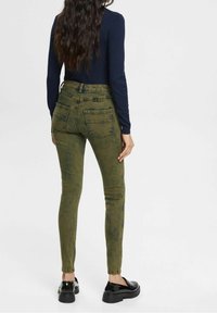 Jeans skinny verdes y texturizados con bolsillos traseros, combinados con calzado negro. Costuras visibles y diseño de cintura alta.
