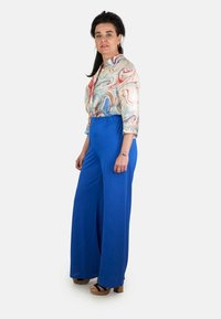 Pantalones azules de corte holgado con cintura alta y banda elástica, combinados con una blusa de mangas largas con un patrón que presenta remolinos de rojo y azul.