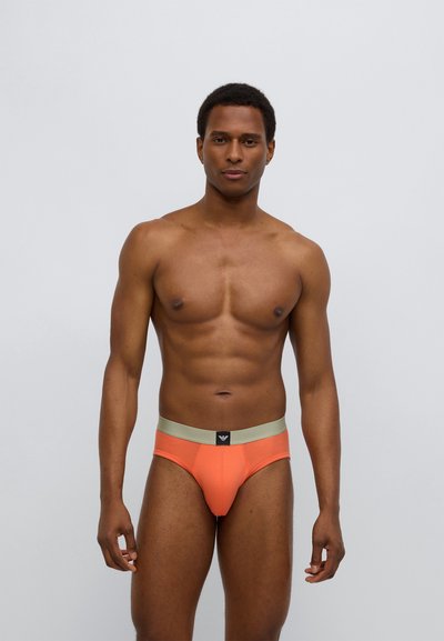 Orange bomullsbriefs med ett ljusgrönt elastiskt midjeband och logotyp, med en åtsittande passform och minimalistisk design. Mjukt textur över hela plagget.