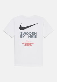 White cotton t-shirt with black Nike logo and gray text "SWOOSH BY NIKE". Features red address details printed on the back. Classic fit.