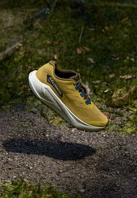 Yellow running shoe with a textured mesh upper, black logo, and blue laces. Features a cushioned white sole and a rounded toe design.