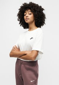 Λευκό βαμβακερό μπλουζάκι με μικρό μαύρο λογότυπο Nike στο στήθος, συνδυασμένο με βουργουνδί φόρμα με λευκό λογότυπο Nike στο μηρό.