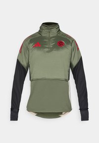 Πράσινο και μαύρο αθλητικό πουλόβερ με υψηλό γιακά, μπροστινό μισό φερμουάρ και κόκκινες λεπτομέρειες, κατασκευασμένο από ύφασμα που απορροφά την υγρασία και διαθέτει λογότυπο.