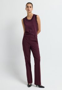 Haut sans manches bordeaux avec bord noir, associé à un pantalon droit assorti. Tissu texturé et design ajusté. Chaussures noires.