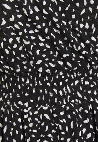 Czarna tkanina z białymi abstrakcyjnymi plamami, z elastycznym ściągaczem w pasie i teksturowaną powierzchnią, tworzącą miękki, lekki wygląd.