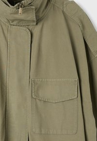 Veste kaki avec une poche avant à rabat, une fermeture éclair et un bouton-pression au col.