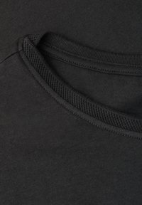Gros plan du col d'un t-shirt noir à col rond montrant des fines coutures et un tissu côtelé texturé autour du col.