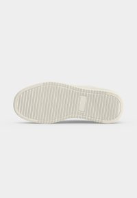 Sål på en hvid sneaker med vandrette riller og et rektangulært tekstureret område i midten, vist på en ensfarvet lys baggrund.