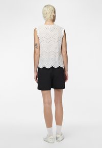 Haut en dentelle blanche avec ourlet festonné, manches courtes et motif floral découpé, associé à un short noir.
