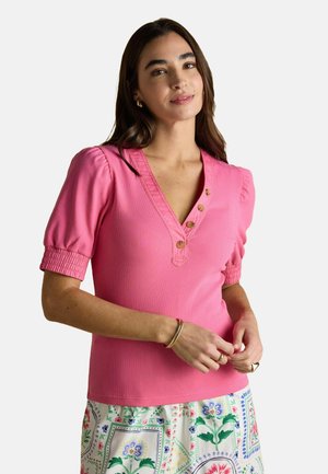 Rosa geripptes Kurzarmoberteil mit V-Ausschnitt, das drei Knopfdetails auf der Vorderseite und geraffte Manschetten aufweist, kombiniert mit einem Blumenrock.