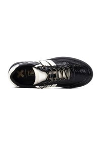 Zapatilla negra con textura brillante de charol, acentos blancos, ojales plateados y punta redondeada. Presenta un cuello acolchado y un diseño de rayas.
