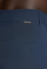 Navy blue shorts made of lightweight fabric feature a back pocket with a flap and a branded tag for Peak Performance.