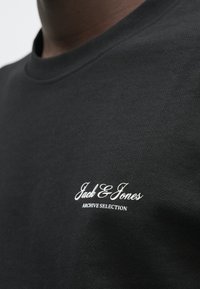 Μαύρο βαμβακερό t-shirt με στρογγυλή λαιμόκοψη, με λευκό κεντητό λογότυπο στο στήθος. Ομαλή υφή με κλασική εφαρμογή και μίνιμαλ σχεδιασμό.