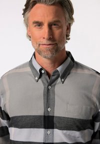 Camisa de botones a cuadros gris y negro con cuello, que presenta un bolsillo con parche y una textura suave. Con dobladillo redondeado y sutiles detalles de botones.