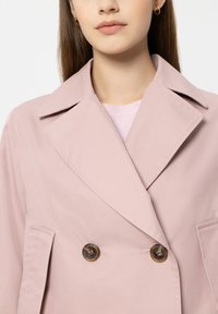 Light pink double-breasted jacket with notched collar, two front pockets, and bronze button accents. Smooth fabric texture.