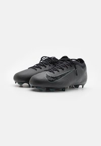 Par de botas de fútbol Nike negras con superficie texturizada y cordones, posicionadas una al lado de la otra sobre un fondo blanco.