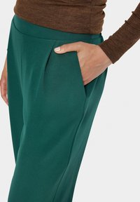 Pantalons verts en tissu lisse avec une coupe ajustée, dotés de poches latérales et de plis subtils à la taille.